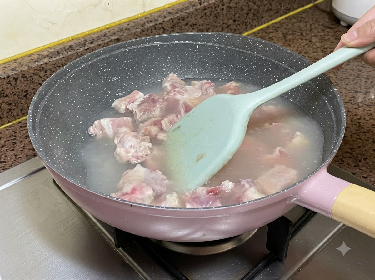 Costine di maiale che bollono nellacqua allinterno di una padella mentre vengono mescolate con una spatola in silicone azzurro.