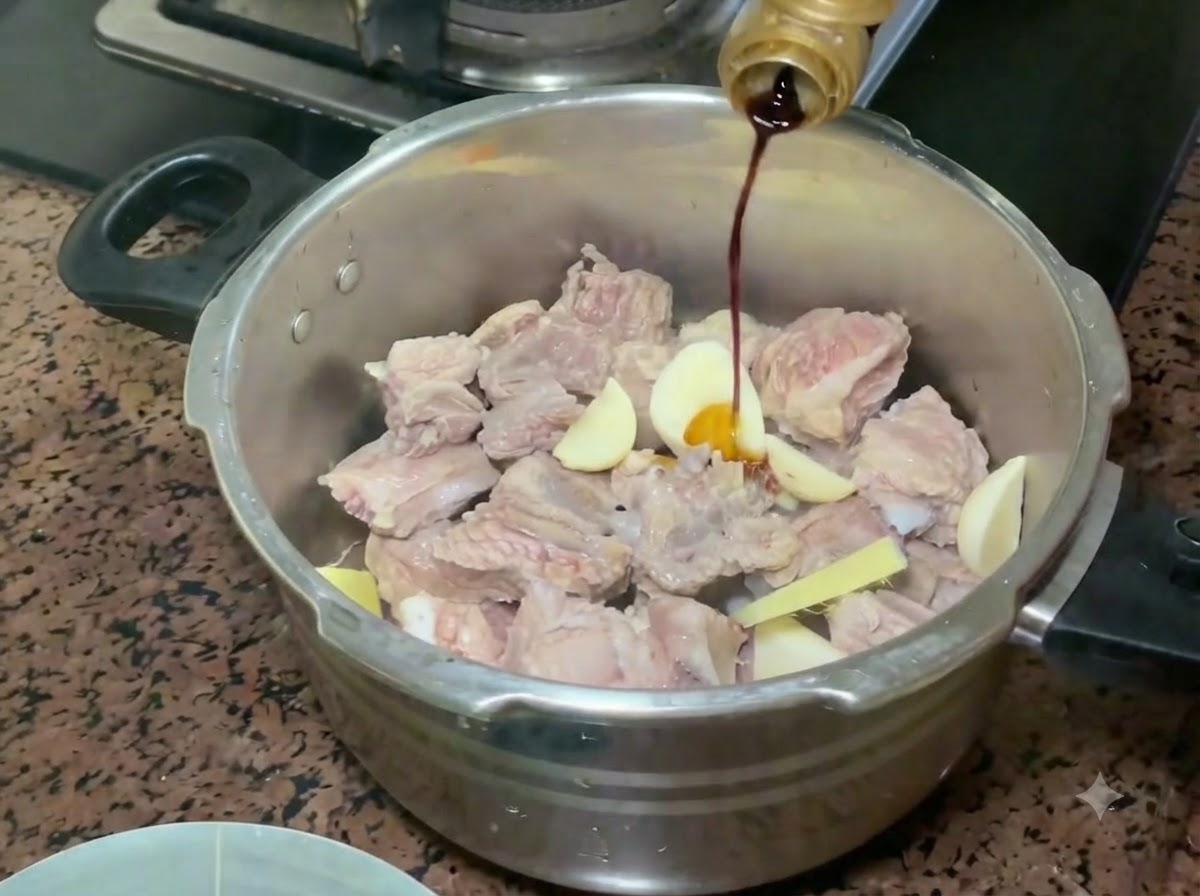Salsa di soia chiara versata da una bottiglia sulle costine di maiale e sugli aromi nella pentola a pressione.