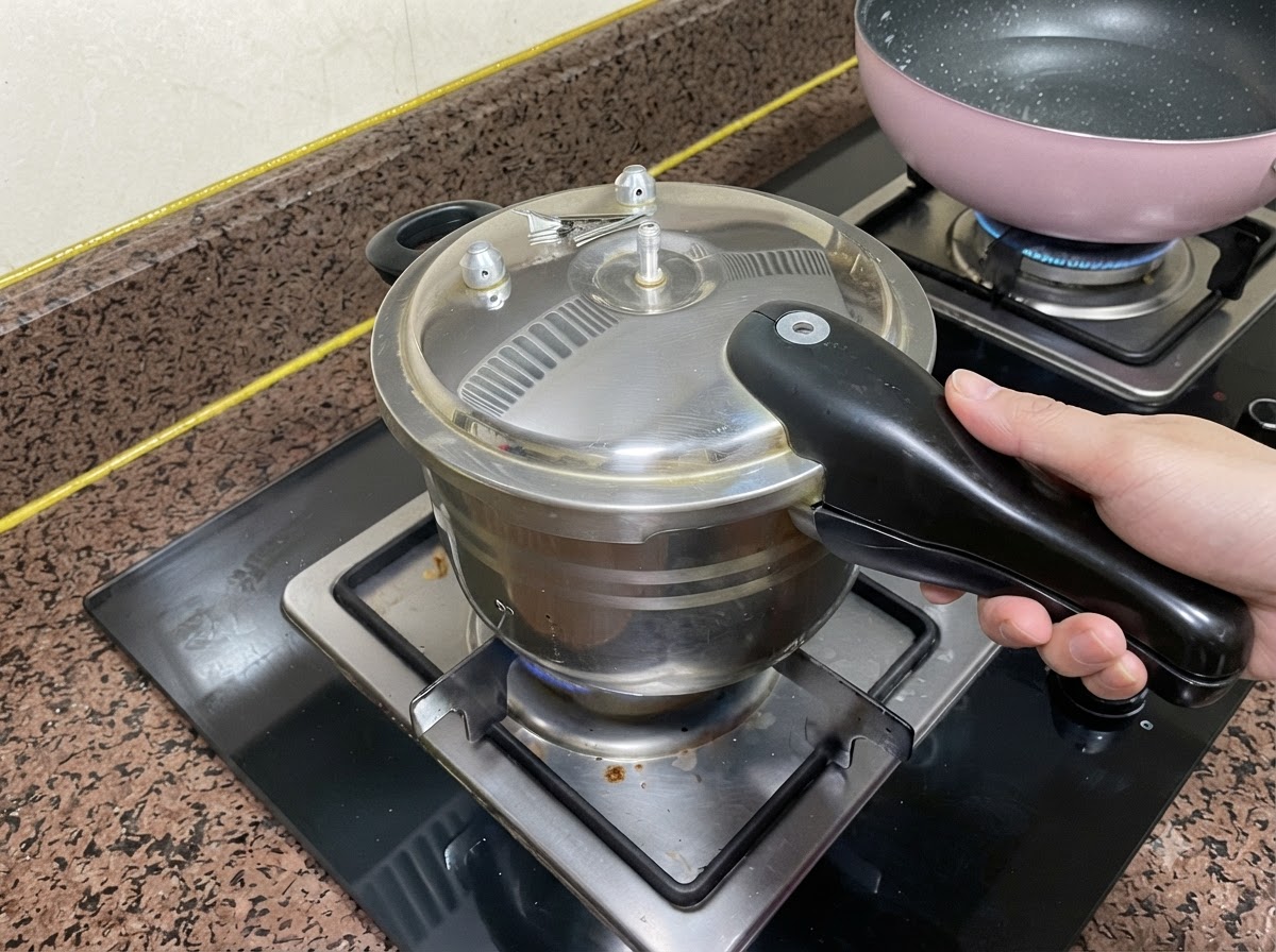 Il coperchio di una pentola a pressione chiuso su un fuoco del piano cottura con una mano che afferra la maniglia.