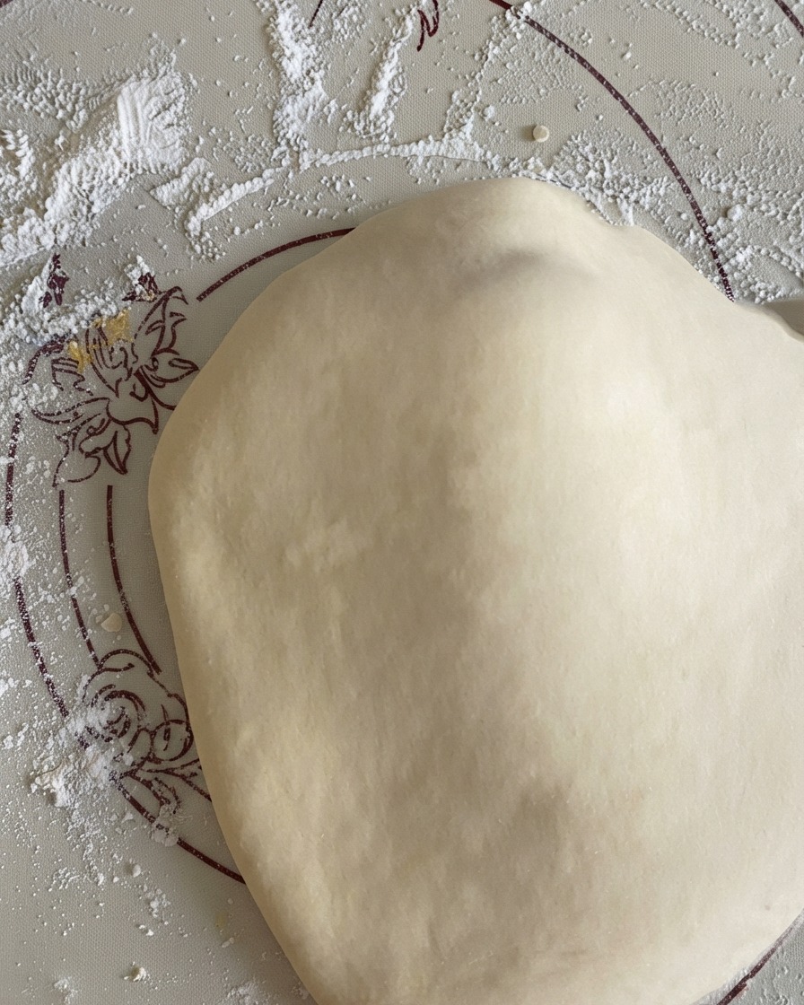 Disco di pasta per pizza allargato e adagiato su un tappetino in silicone infarinato.