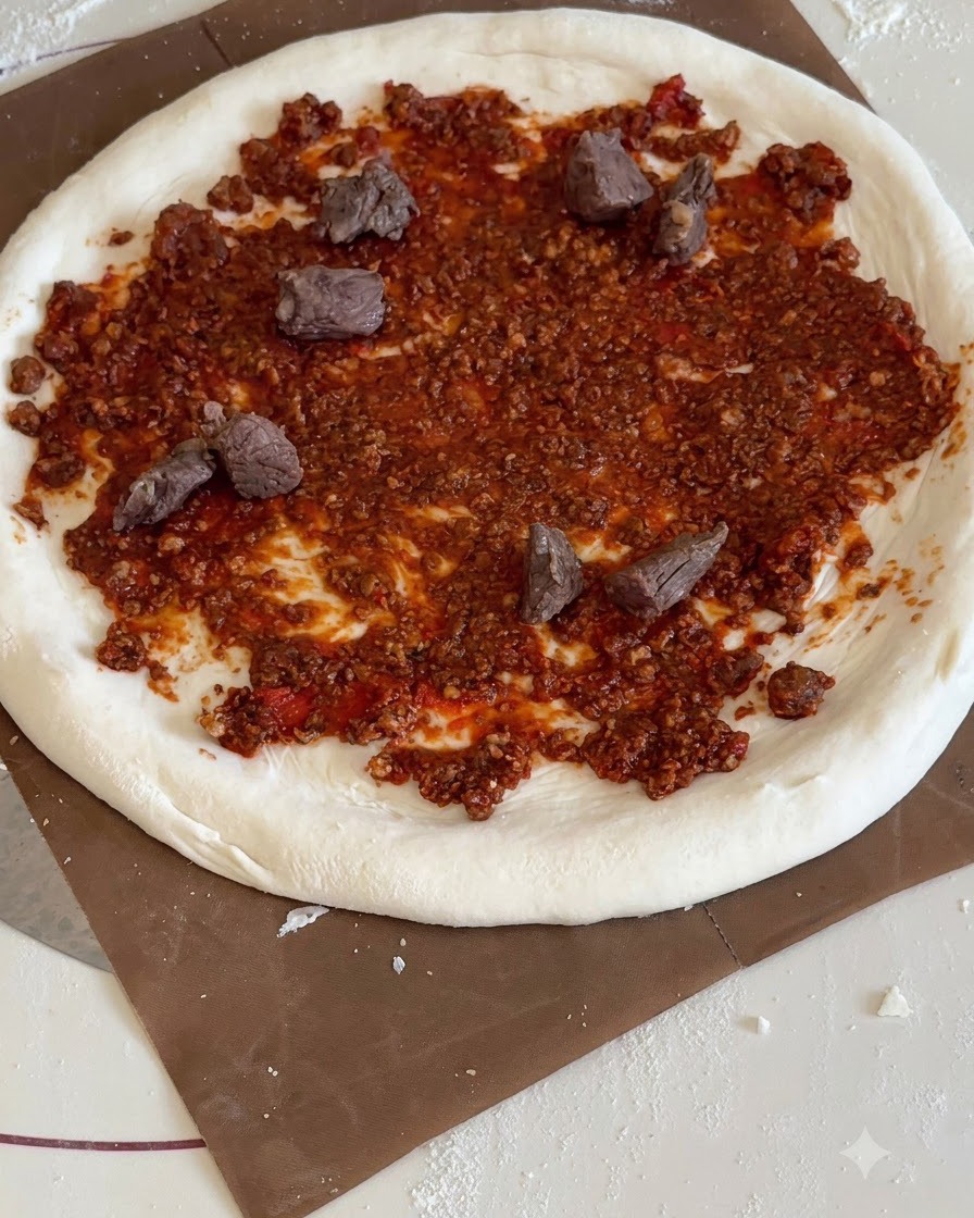 Pezzetti triangolari di ananas giallo e carne di manzo cotta distribuiti sulla base rossa della pizza.
