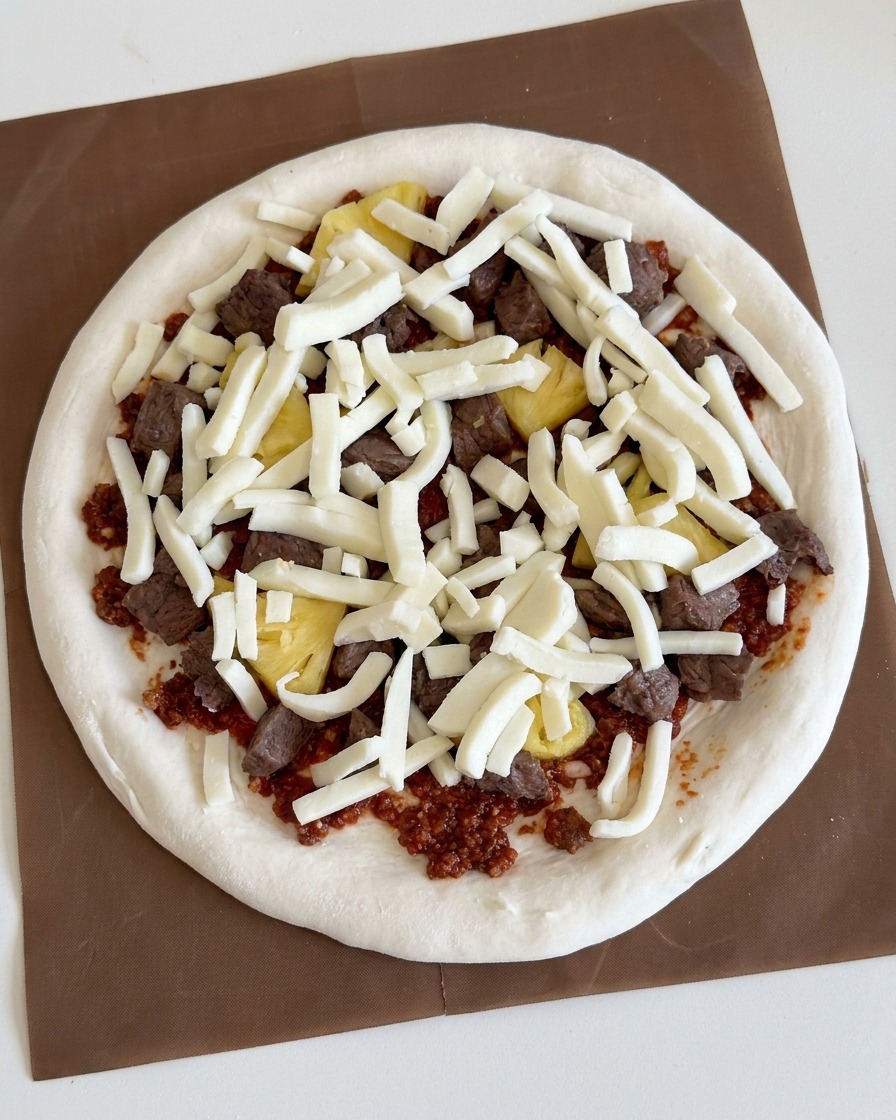 Mozzarella grattugiata bianca cosparsa generosamente sul condimento di carne e ananas.