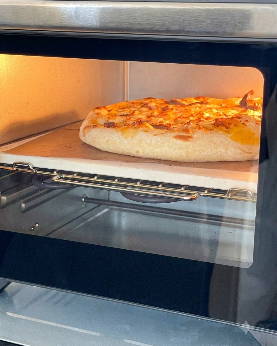 Una pizza dorata e cotta, con formaggio fuso, dentro un fornetto elettrico su pietra refrattaria.