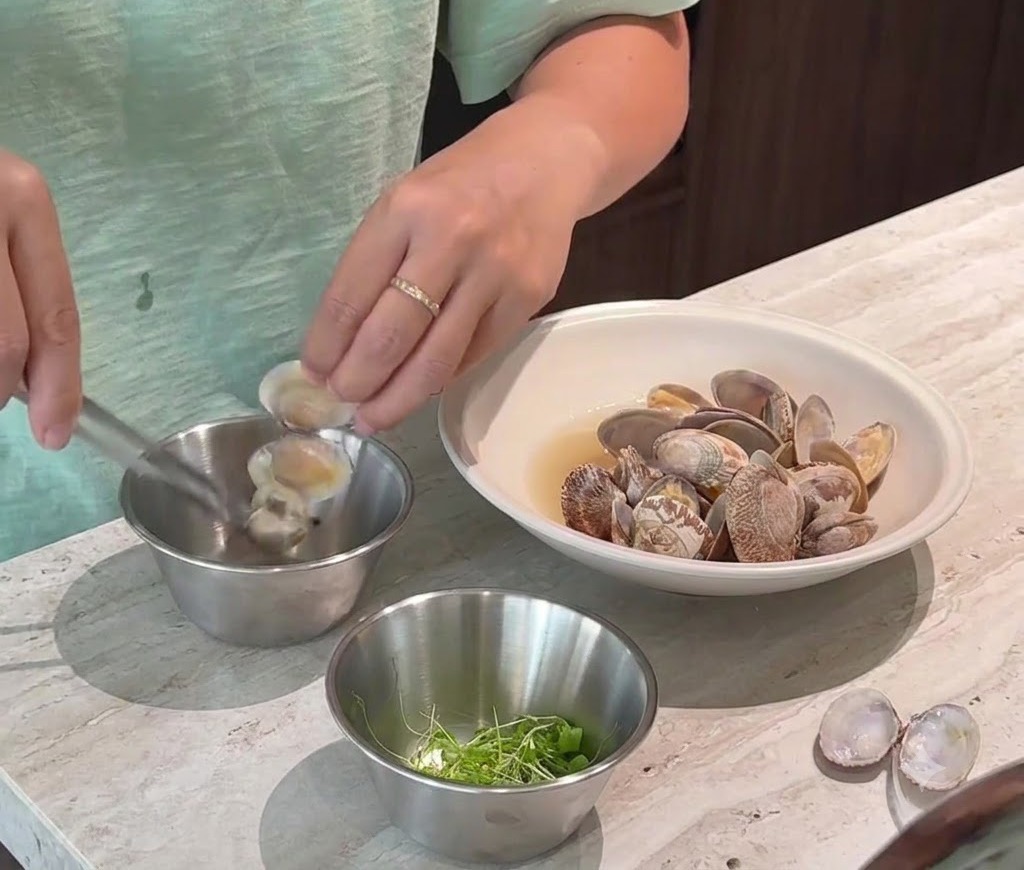 Una persona che rimuove con cura la polpa cotta delle vongole dai gusci e la mette in una piccola ciotola di metallo.