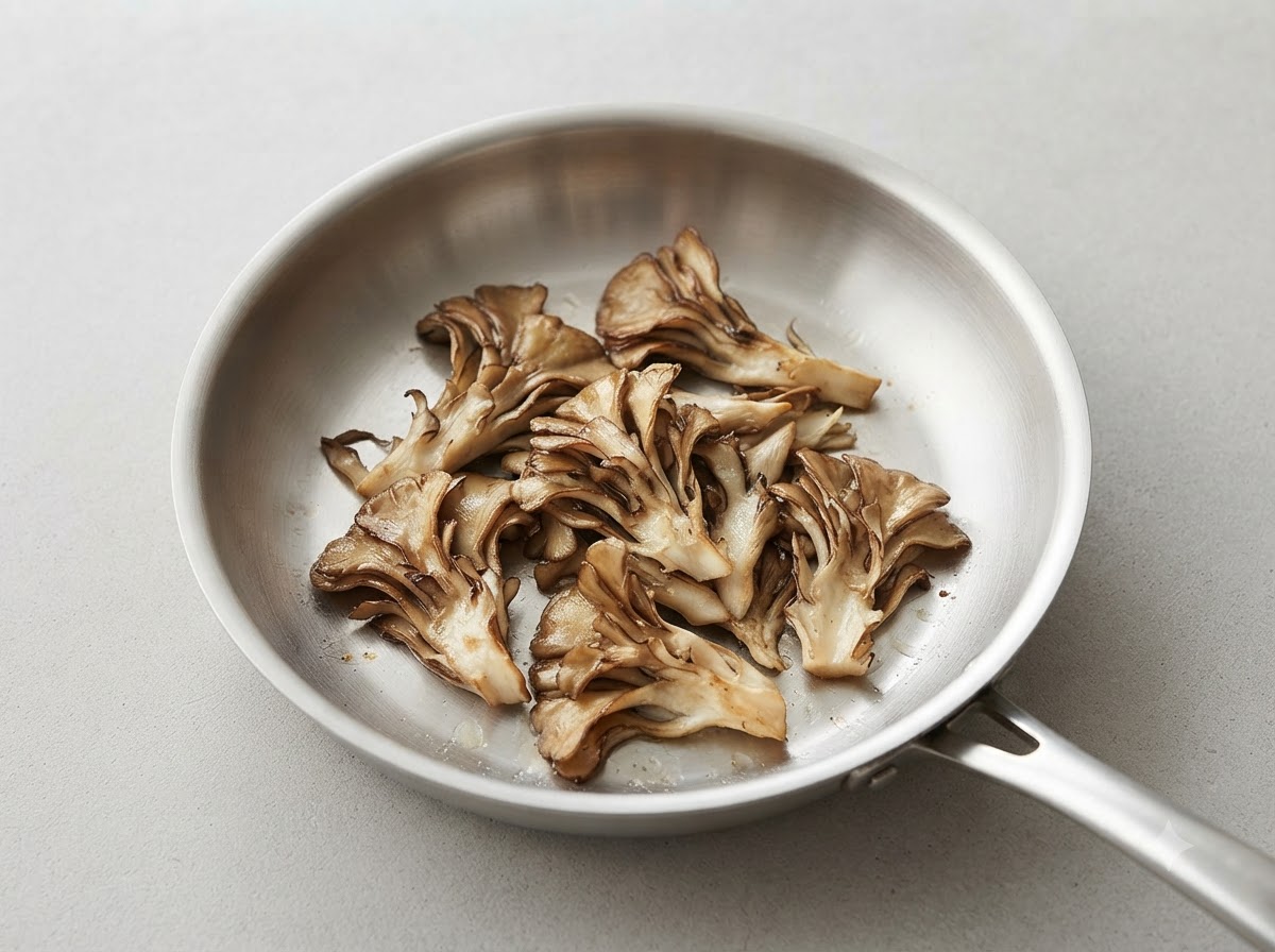 Pezzi strappati di funghi maitake che dorano in una padella di acciaio inossidabile pulita.