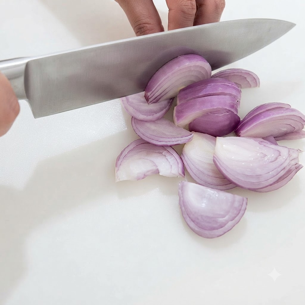 Mani che affettano e tagliano a cubetti una mezza cipolla rossa con un coltello da chef su un tagliere bianco.