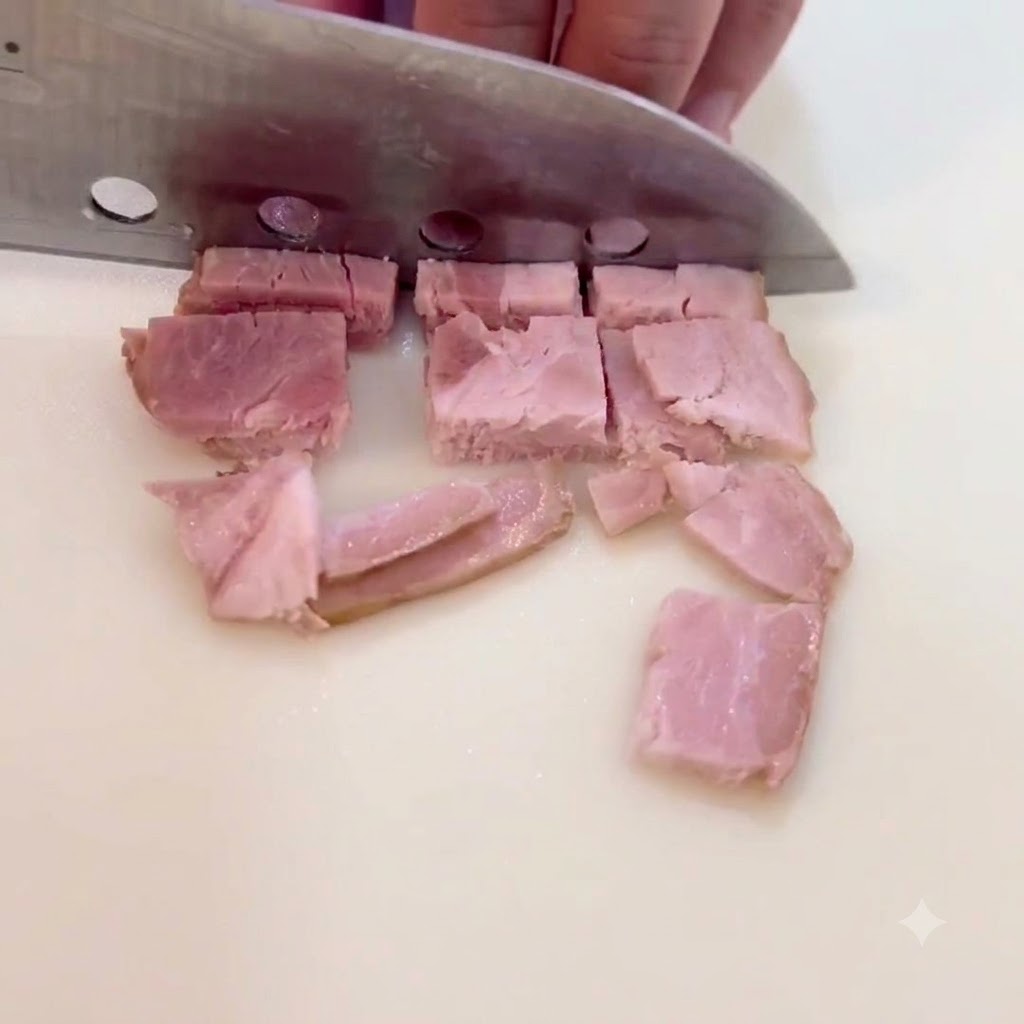 Fette di pancetta tagliate a quadratini su una superficie di taglio.