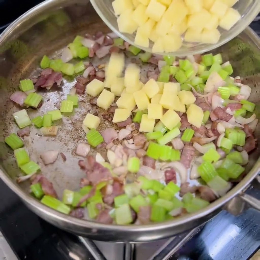 Patate a cubetti versate da una ciotola in una padella contenente cipolle, sedano e pancetta.