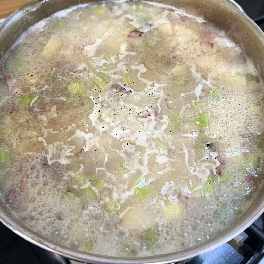 Una pentola di zuppa in cottura a fuoco lento, punteggiata di pepe nero sulla superficie in ebollizione.