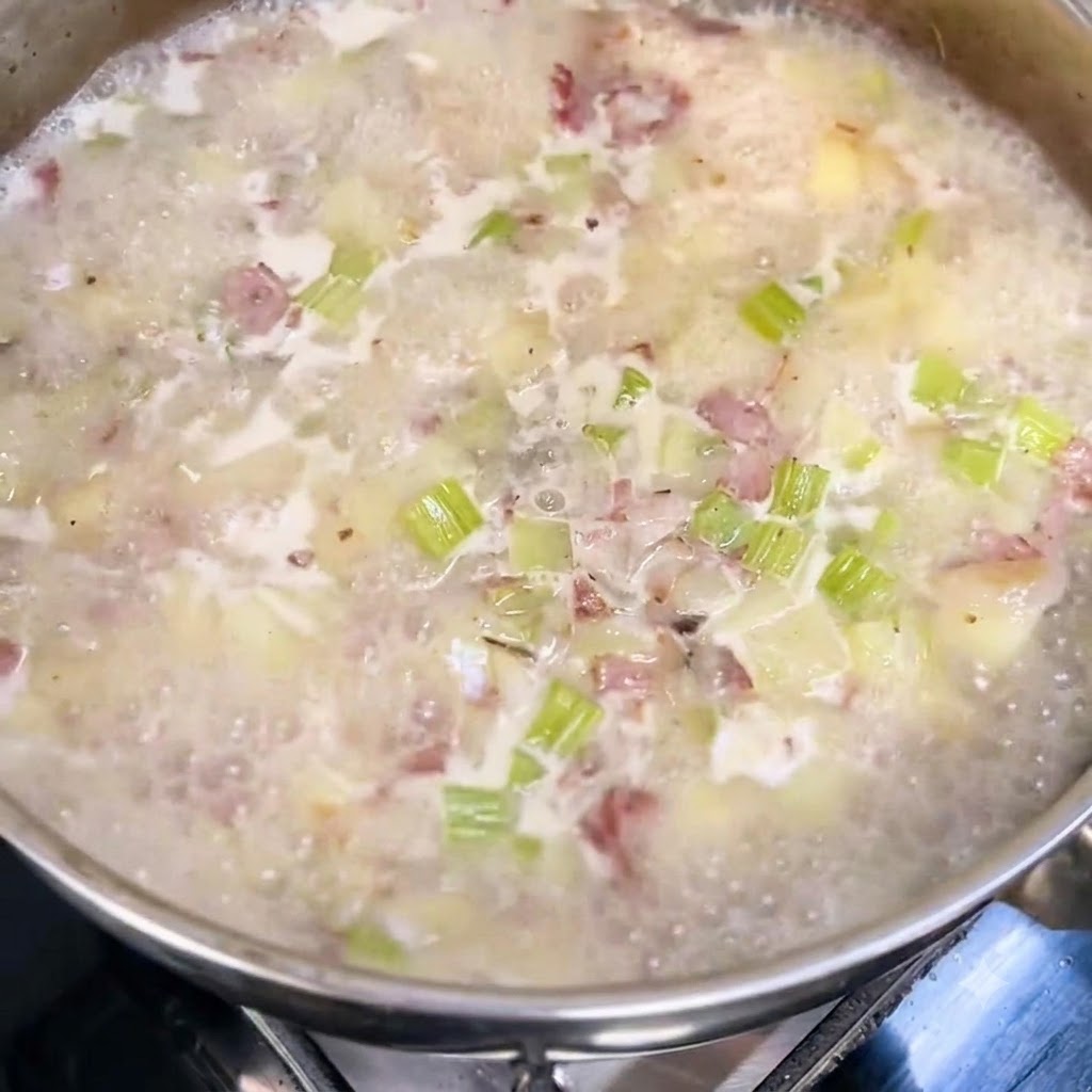 Latte e panna versati in una pentola in leggera ebollizione con patate, sedano e pancetta.