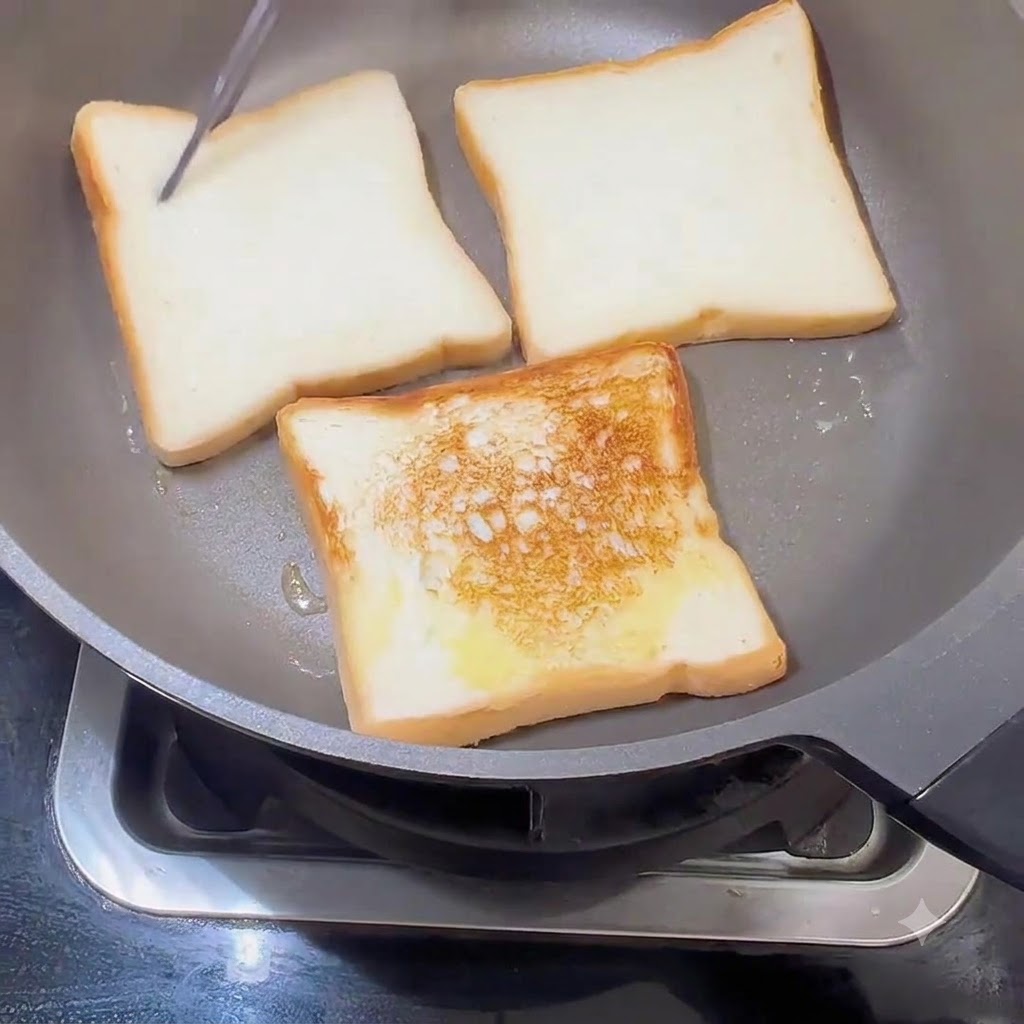 Fette di pane girate in una padella, che mostrano una crosta dorata su un lato.