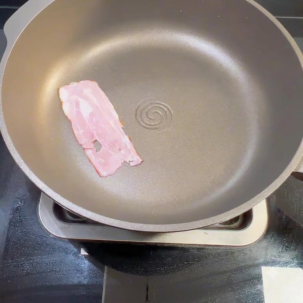 Una striscia di pancetta cruda posizionata in piano allinterno di una padella asciutta sui fornelli.