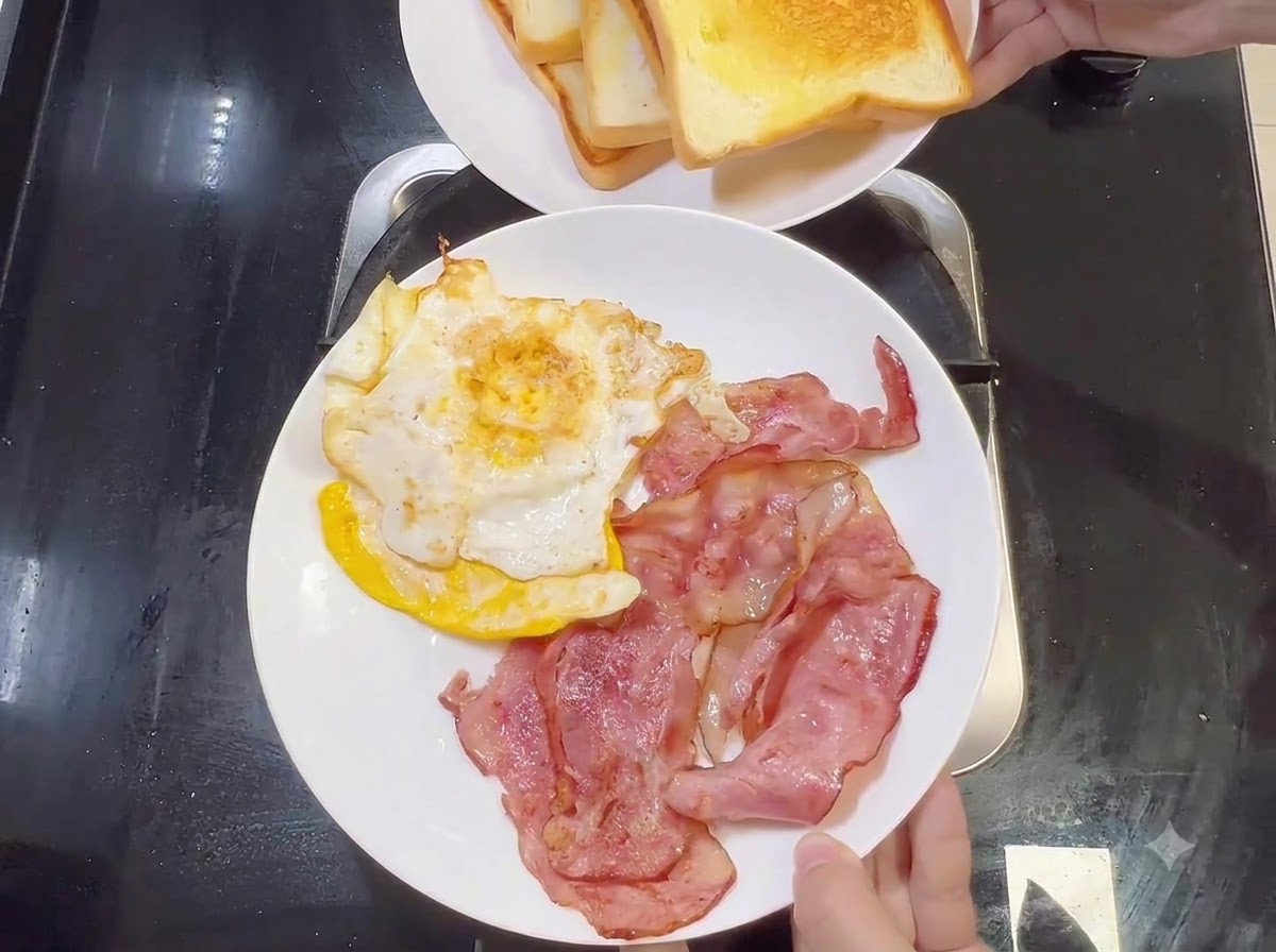 Un piatto bianco con strisce di pancetta cotta e uova fritte, con un altro piatto di pane tostato tenuto sopra.