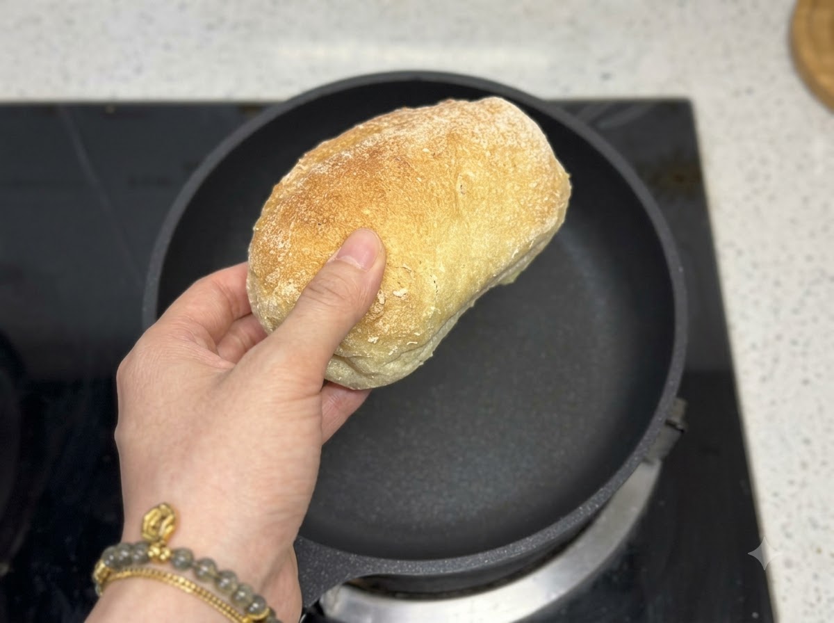 Una mano che tiene una pagnotta di ciabatta direttamente sopra una padella nera vuota.