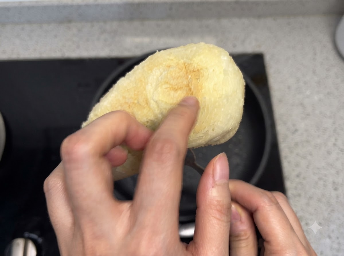 Una mano che preme sulla superficie inferiore di un pezzo di pane tostato per verificarne la croccantezza.