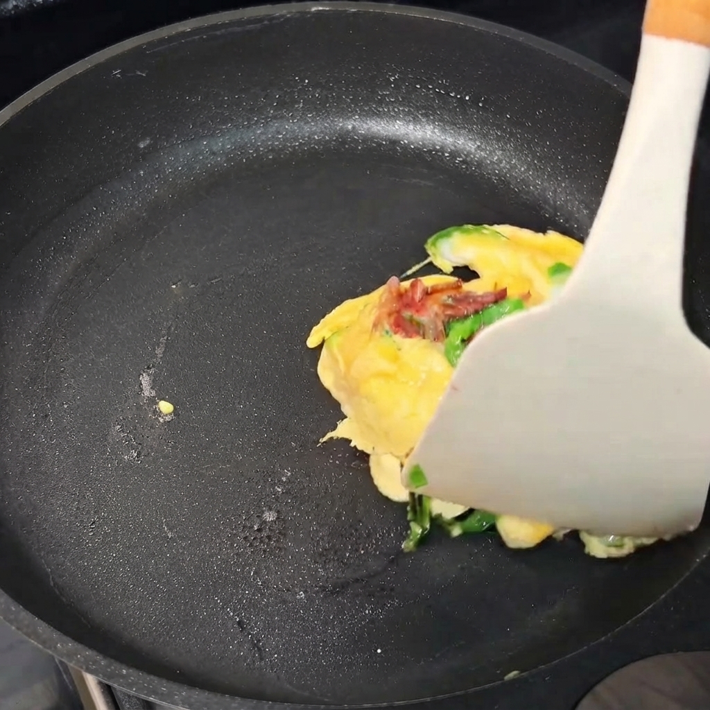Un pacchetto di frittata di uova che viene piegato con una spatola allinterno di una padella.