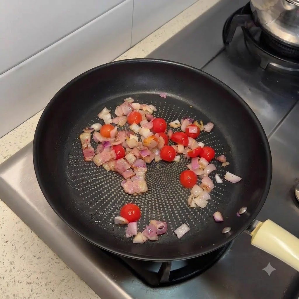 Una padella riempita con pancetta rosolata, cipolle tritate e pomodorini tagliati a metà.