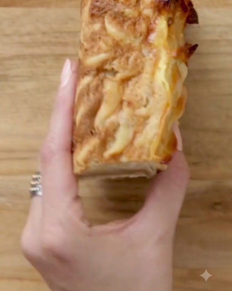Una mano che tiene una porzione quadrata di kugel tagliata ordinatamente su un tagliere di legno.