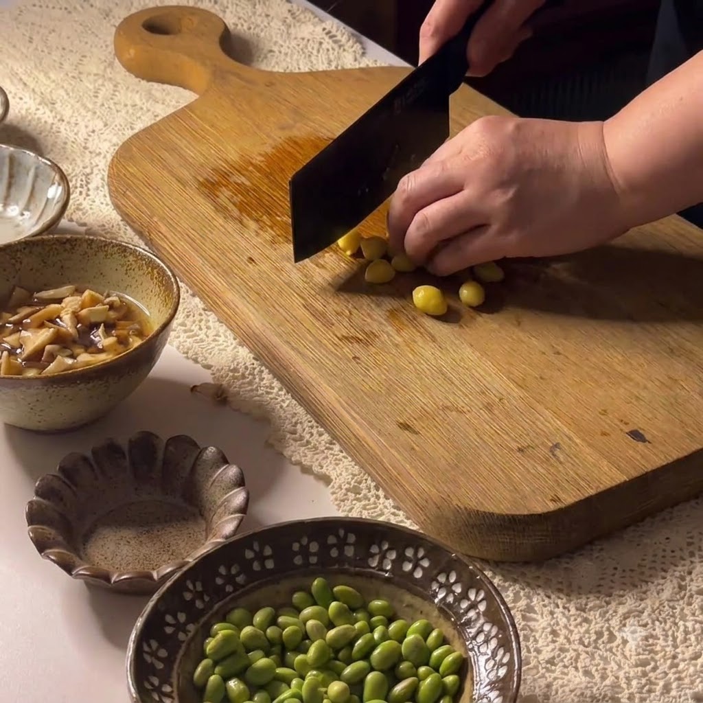 Noci di ginkgo tagliate su un tagliere di legno con una mannaia.