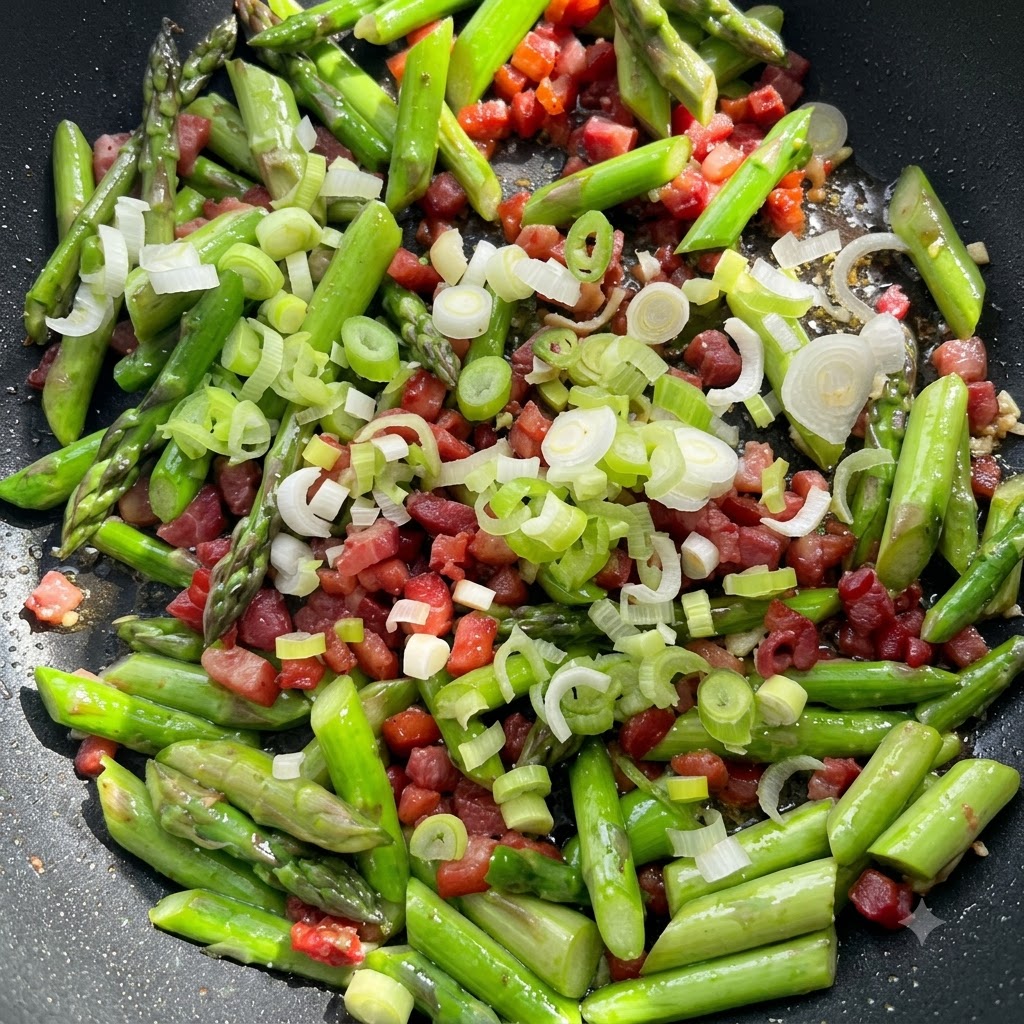Aglio tritato finemente e parti bianche di cipollotto sparse sopra gli asparagi e la pancetta in padella.