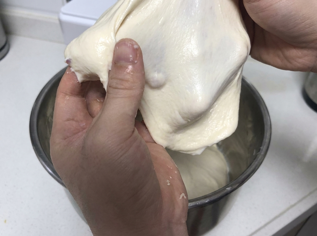 Mani che tirano e allungano un pezzo morbido di impasto bianco elastico per dimostrare la forza del glutine.