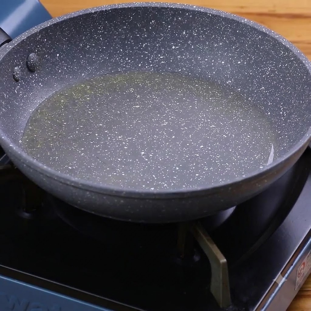 Aglio e peperoni verdi che friggono in olio caldo allinterno di una padella maculata.
