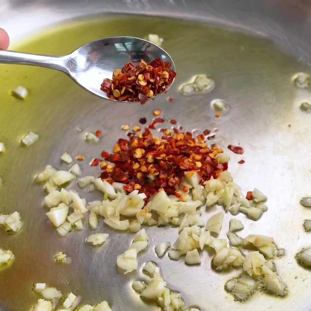 Aglio tritato e fiocchi di peperoncino che sfrigolano in una padella in acciaio con olio doliva.