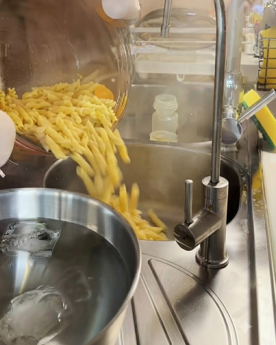 Pasta fusilli cotta che viene scolata in uno scolapasta di metallo sopra una ciotola di acqua ghiacciata.