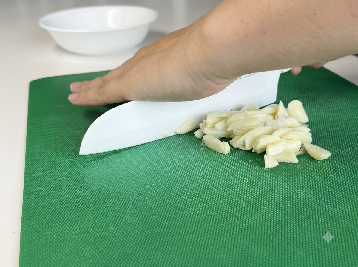 Spicchi daglio tritati finemente su un tagliere usando un coltello bianco.