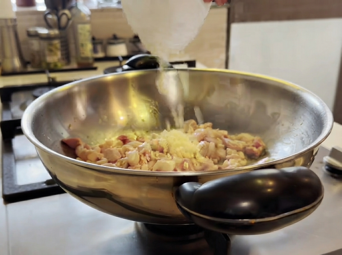 Aglio tritato aggiunto in un wok con il pollo in cottura e mescolato con una spatola.