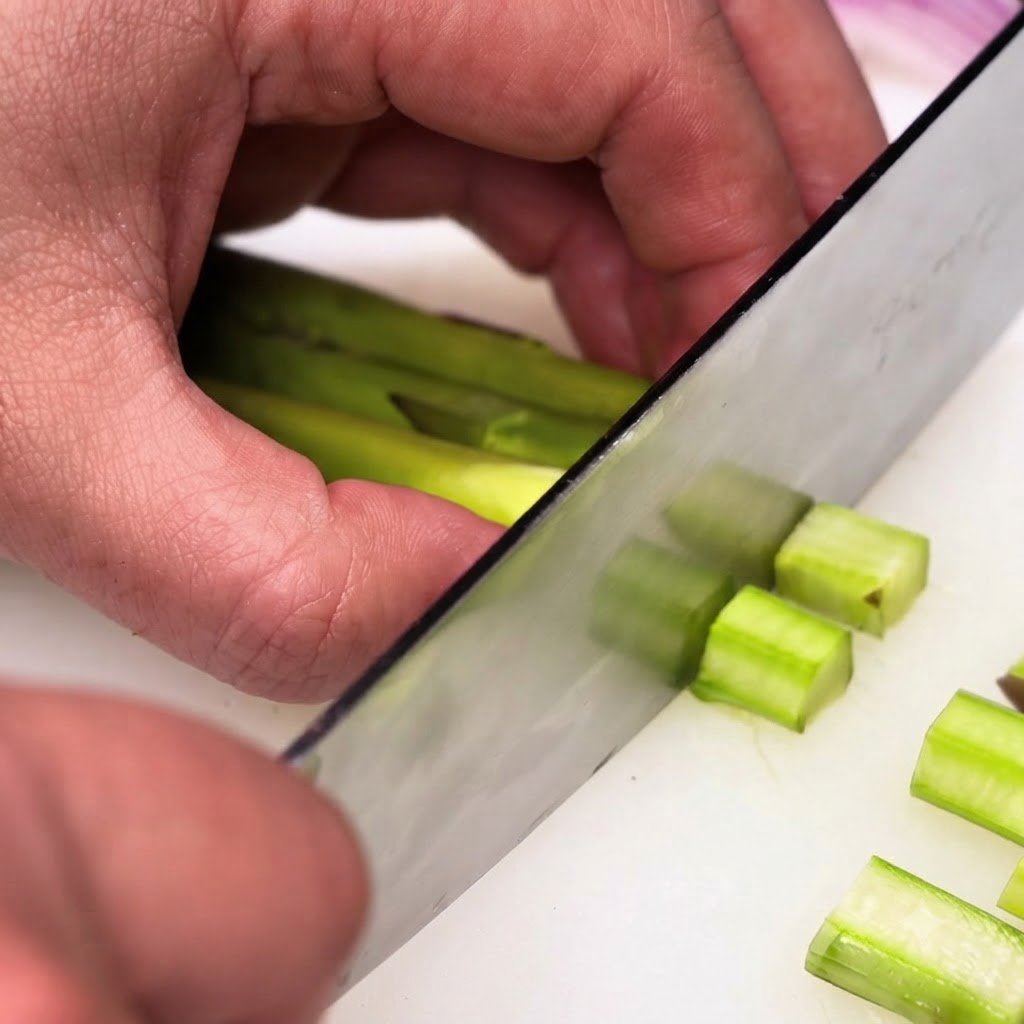 Gambi di asparagi verdi pelati tagliati a piccoli pezzi uniformi con un coltello da cucina.