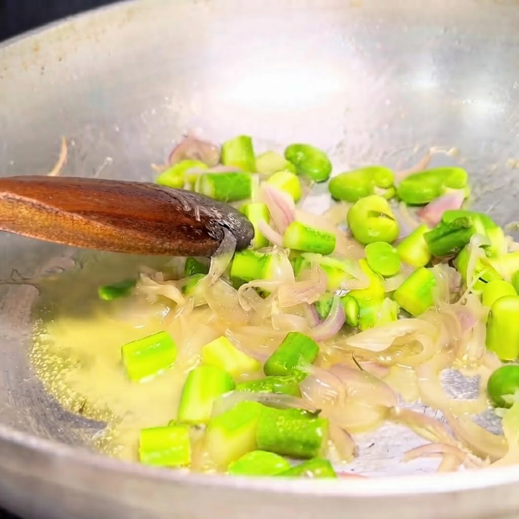 Cipolle saltate e verdure verdi raccolte da una padella in metallo con un cucchiaio di legno.