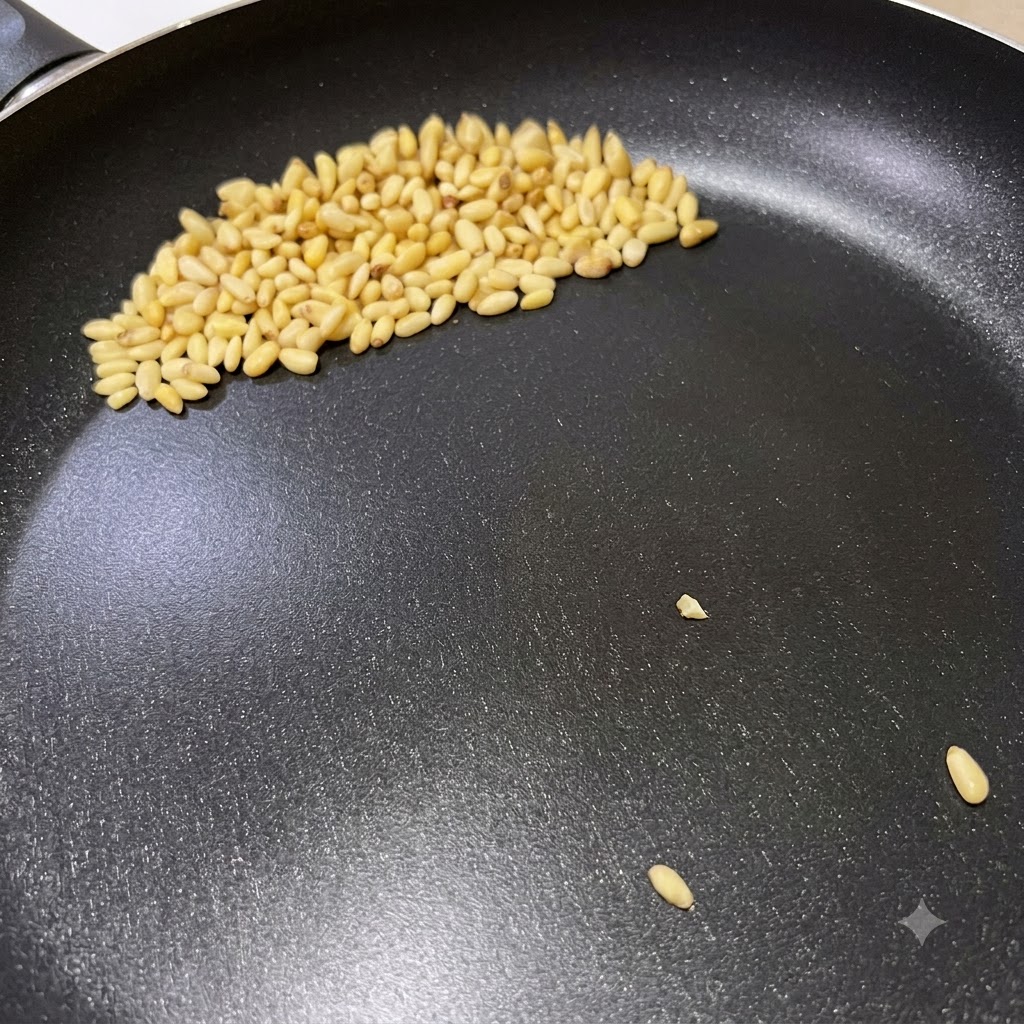Pinoli che dorano in una padella asciutta durante la preparazione della pasta al pesto italiano.