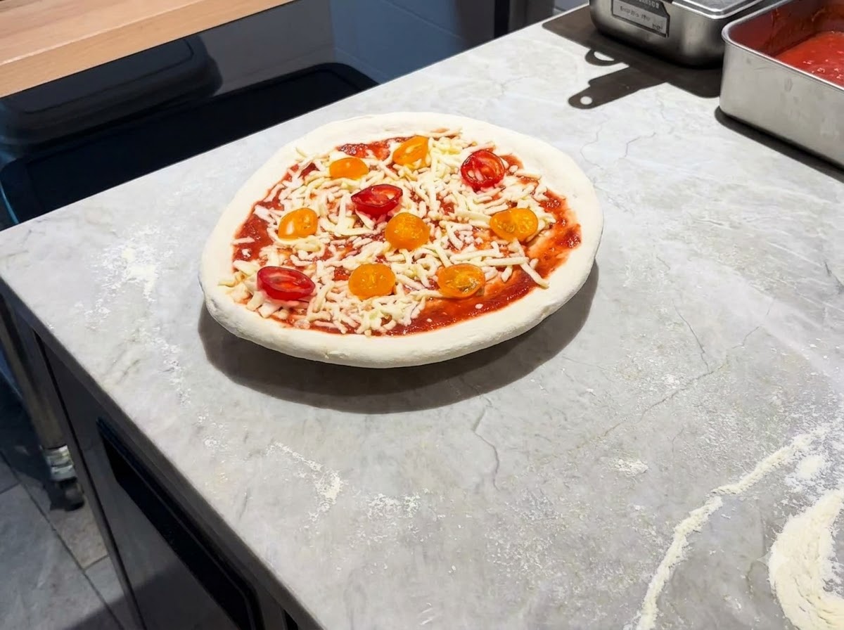Una pizza completamente assemblata che poggia su una pala di metallo su un piano di marmo.