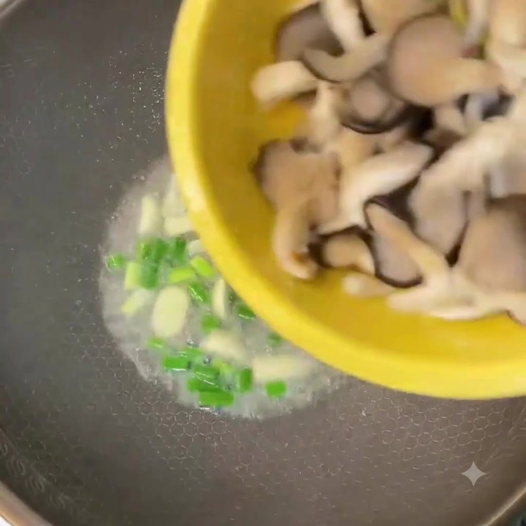Funghi oyster tagliati versati da una ciotola gialla in un wok con cipollotti e aglio.