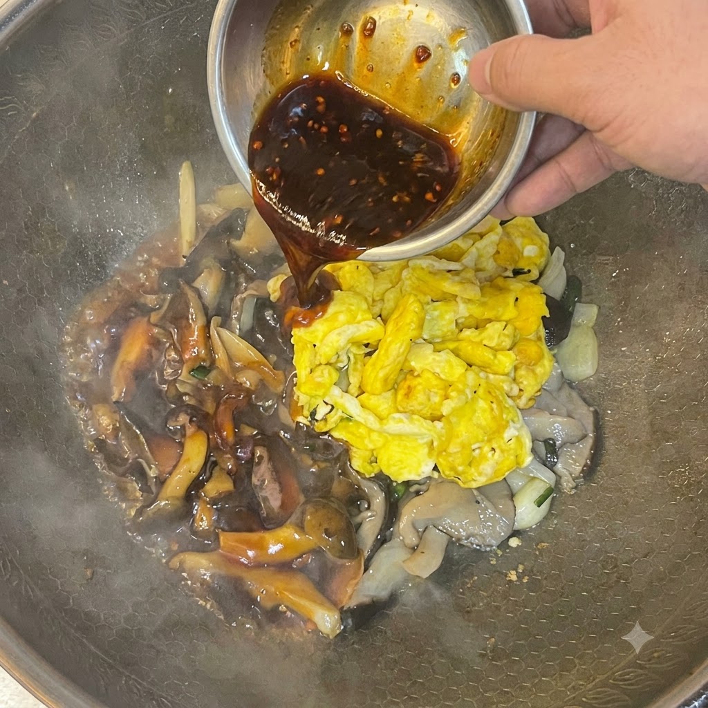 Salsa scura versata da una ciotola di metallo sopra le uova strapazzate e i funghi in un wok.