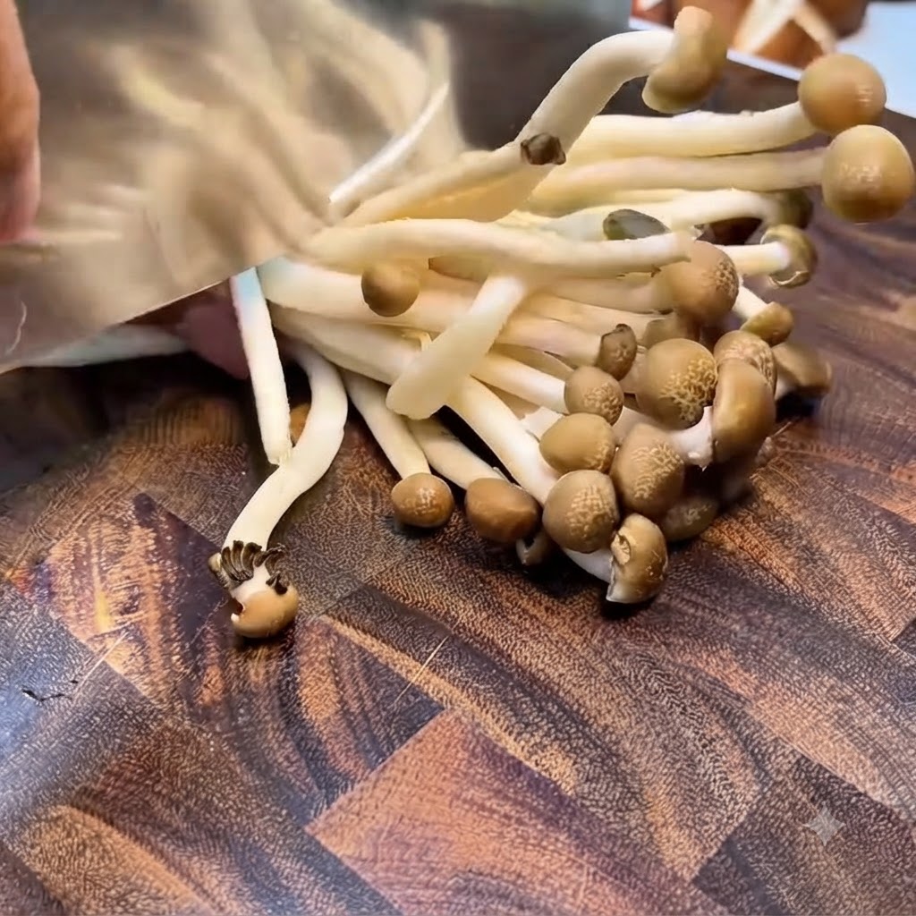 Funghi shimeji tagliati alla base della radice con una mannaia su un asse di legno.
