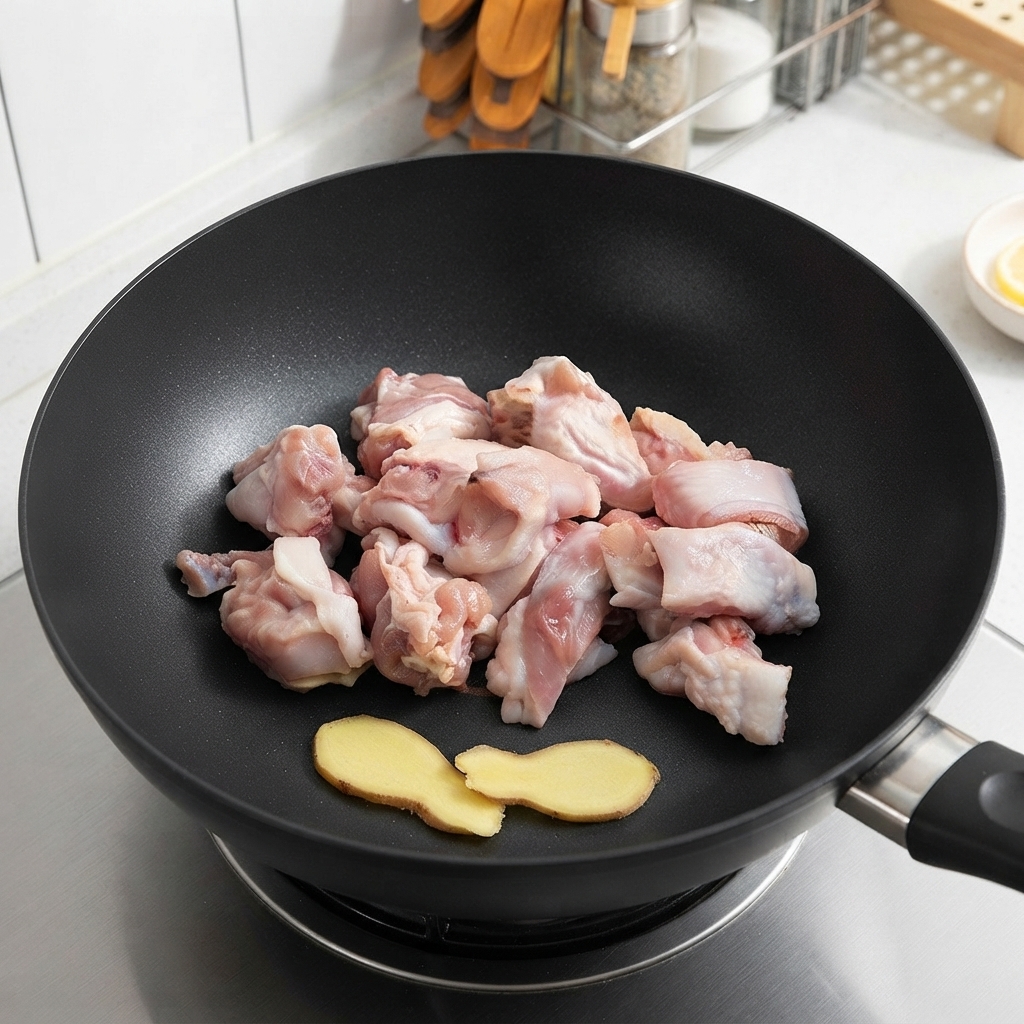 Pezzi di pollo crudo e fette di zenzero adagiati in un wok prima della frittura.