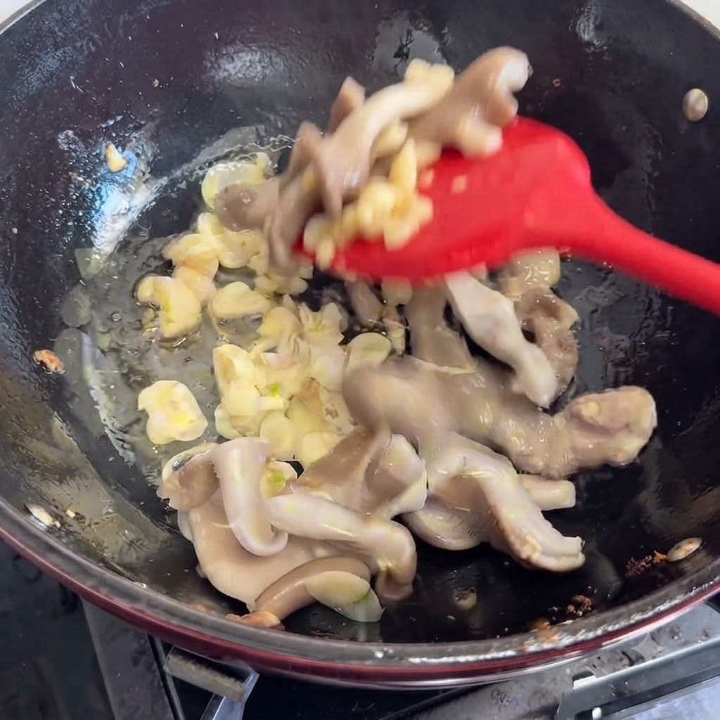 Funghi freschi aggiunti e mescolati nella padella con gli aromi usando una spatola rossa.