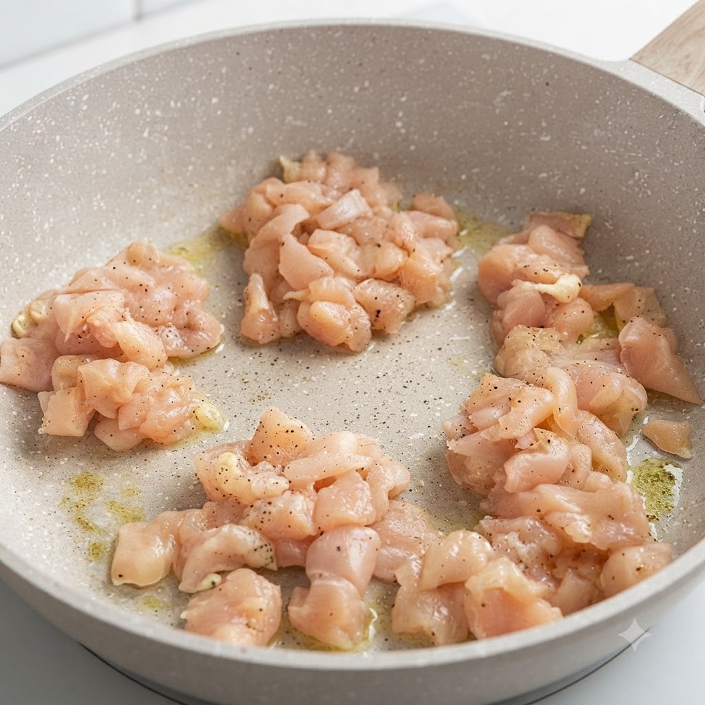 Pezzi di petto di pollo marinato che sfrigolano in una padella rotonda a fuoco basso.