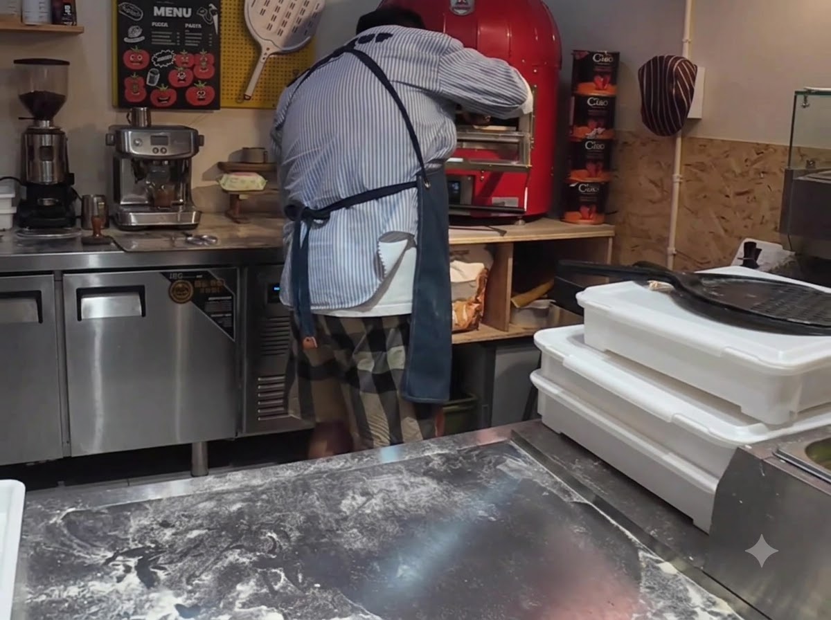 Una pizza che viene inserita in un forno elettrico commerciale rosso brillante utilizzando una pala.