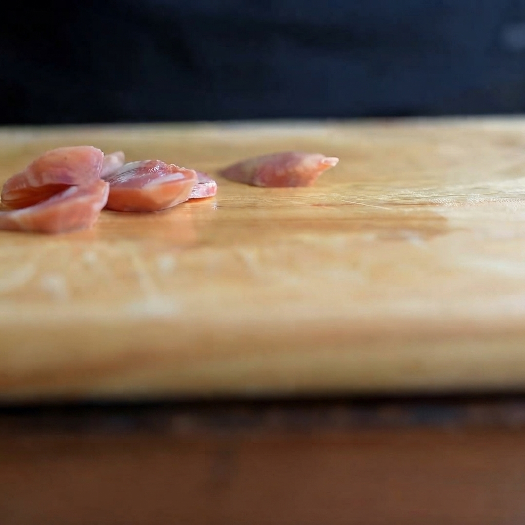 Spicchi daglio affettati sottilmente adagiati su un tagliere di legno.