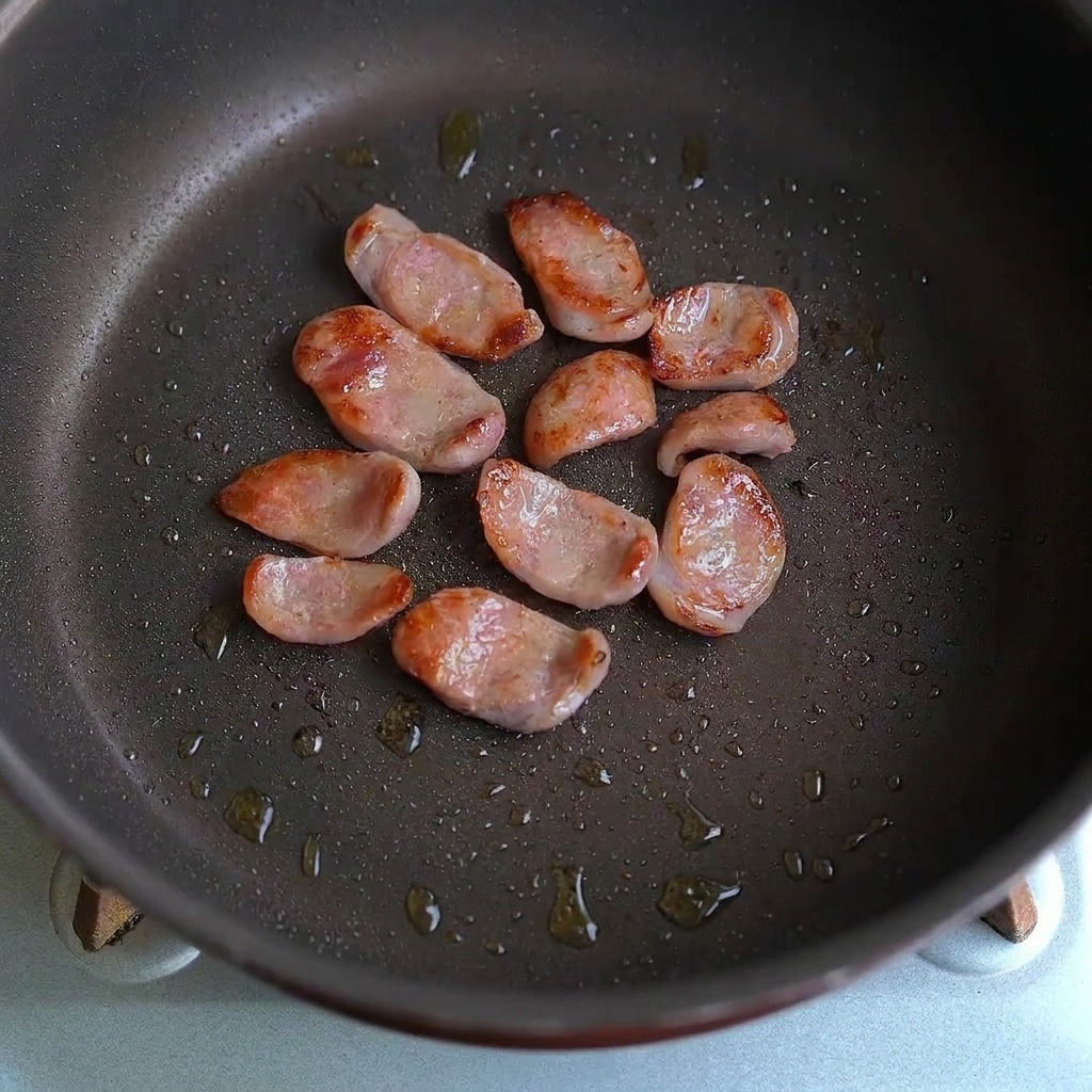 Fette di salsiccia e pezzi daglio saltati insieme in una padella.