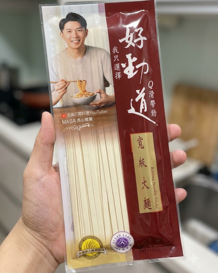Una confezione di bastoncini di noodle larghi Hao Jin Dao tenuta davanti a uno sfondo da cucina.