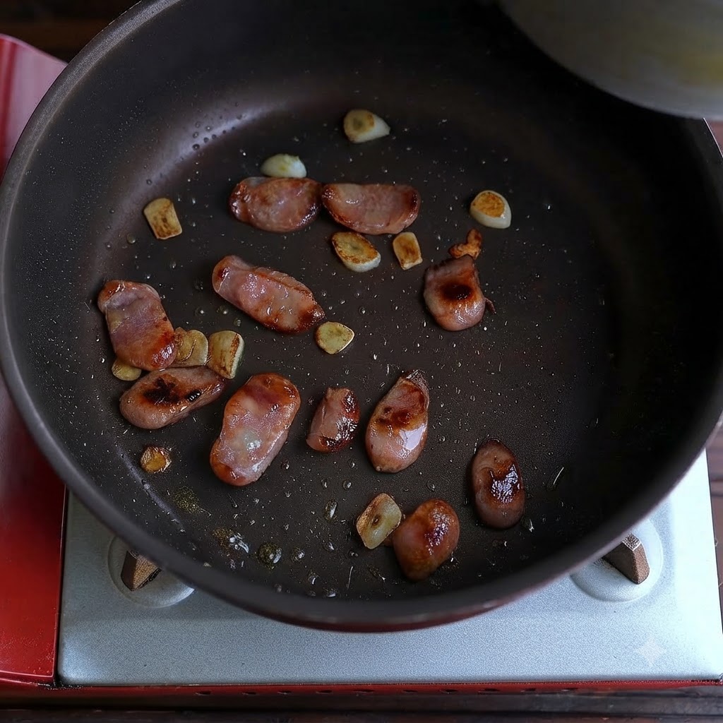 Salsiccia cotta e pezzi daglio fritti sparsi sul fondo di una padella.