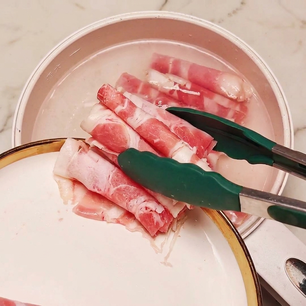 Fettine di manzo surgelate immerse in una pentola di acqua bollente con pezzi di cipollotto usando delle pinze da cucina.