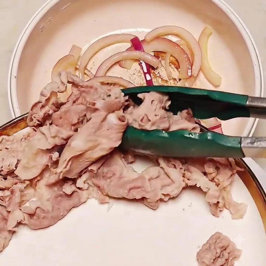 Fette di manzo sbollentate trasferite con le pinze in una padella contenente le cipolle rosolate.