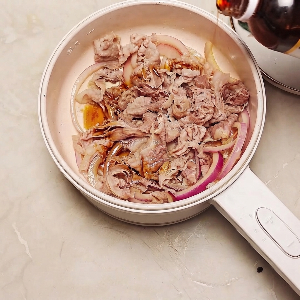 Salsa sukiyaki versata da una bottiglia in una padella piena di manzo e fette di cipolla rossa.