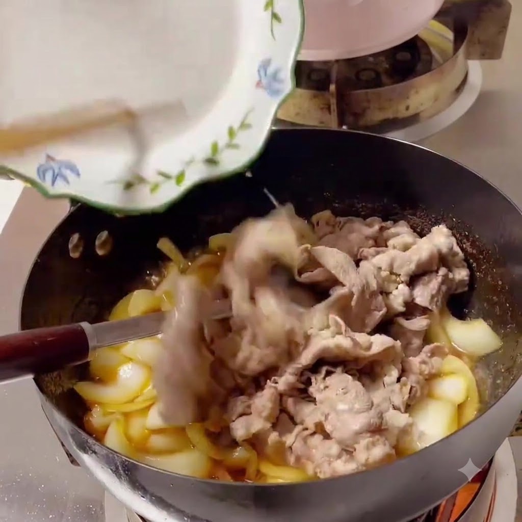 Fettine di manzo cotte fatte scivolare da un piatto bianco in un wok pieno di cipolle e salsa.