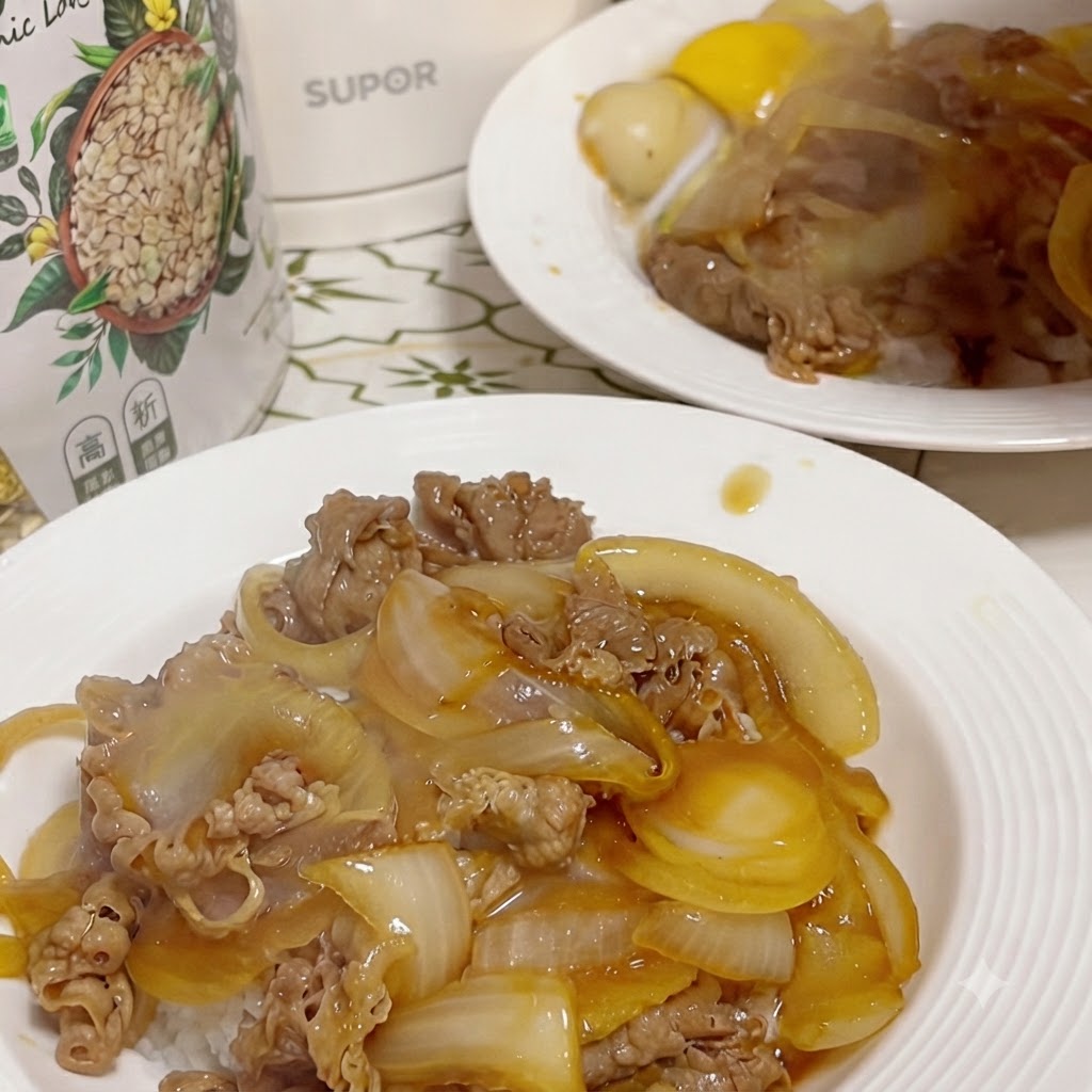 Un piatto finito di manzo e cipolla su riso, con un tuorlo duovo crudo sgusciato sistemato in una piccola fossetta creata al centro, e un secondo piatto visibile sullo sfondo.